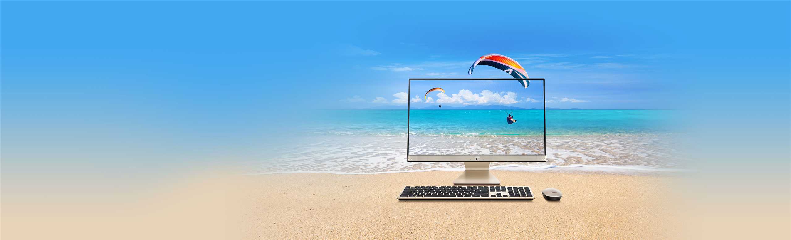 The ASUS AiO M241 display monitor with a keyboard and mouse in a beach setting with two parasailers in the background by the sandy water