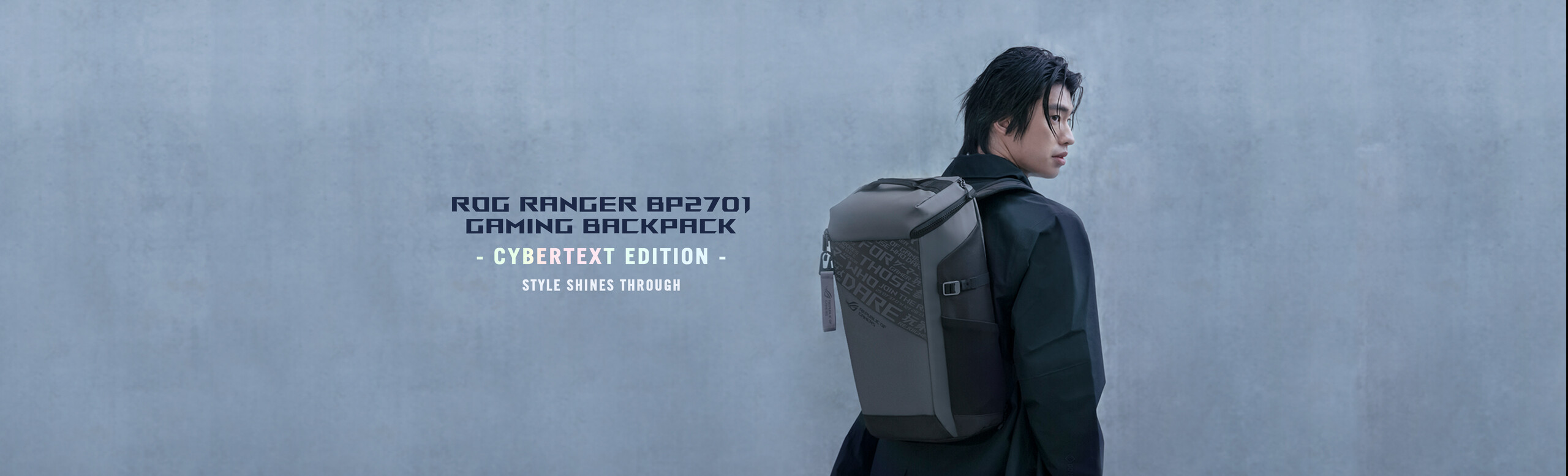 A person with a dark jacket standing near a concrete wall, looking over his shoulder and wearing an ROG Ranger BP2701 Gaming Backpack.