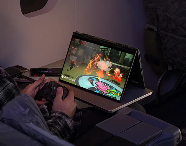 A man with headphones on, riding an airplane, enjoying a controller based game on the Flow X13.