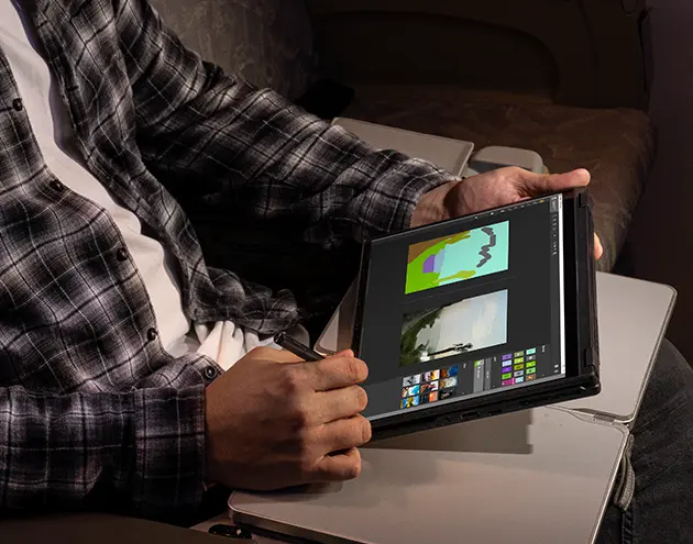 A man sitting on a plane, with the tray table extended, drawing with the Flow X13 in tablet mode.
