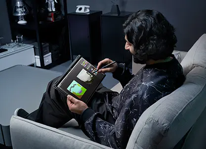 A man sitting on a couch, drawing with the Flow X13 in tablet mode.
