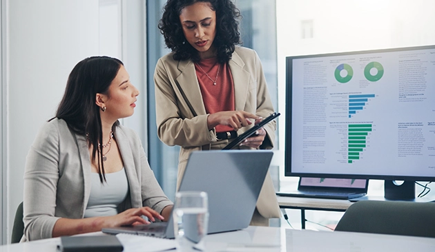 Two business professionals discussing data insights beside a computer screen displaying charts.