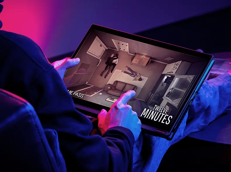 The ROG Flow X16 laptop resting on a desk with a person holding up the laptop screen with his left hand while playing video on the screen with right hand.