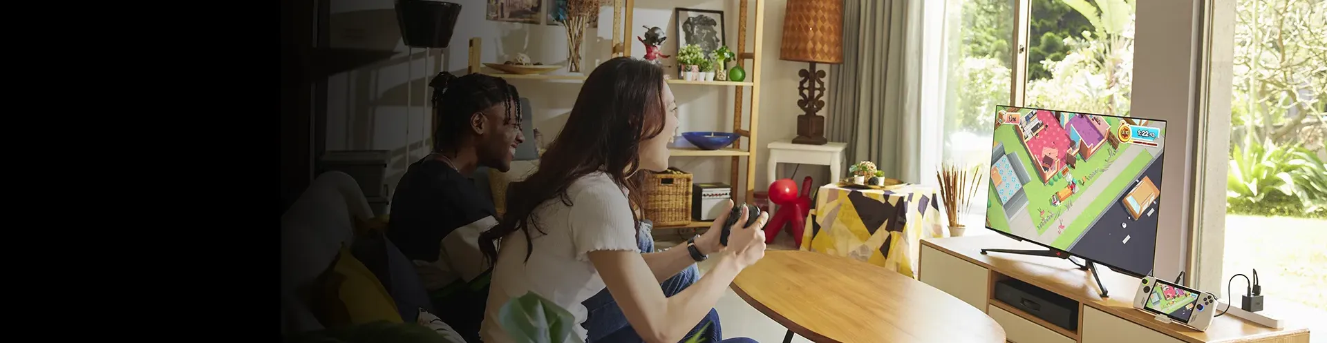 Two people are holding controllers in front of a big TV screen with ROG ALLY conncted to it.