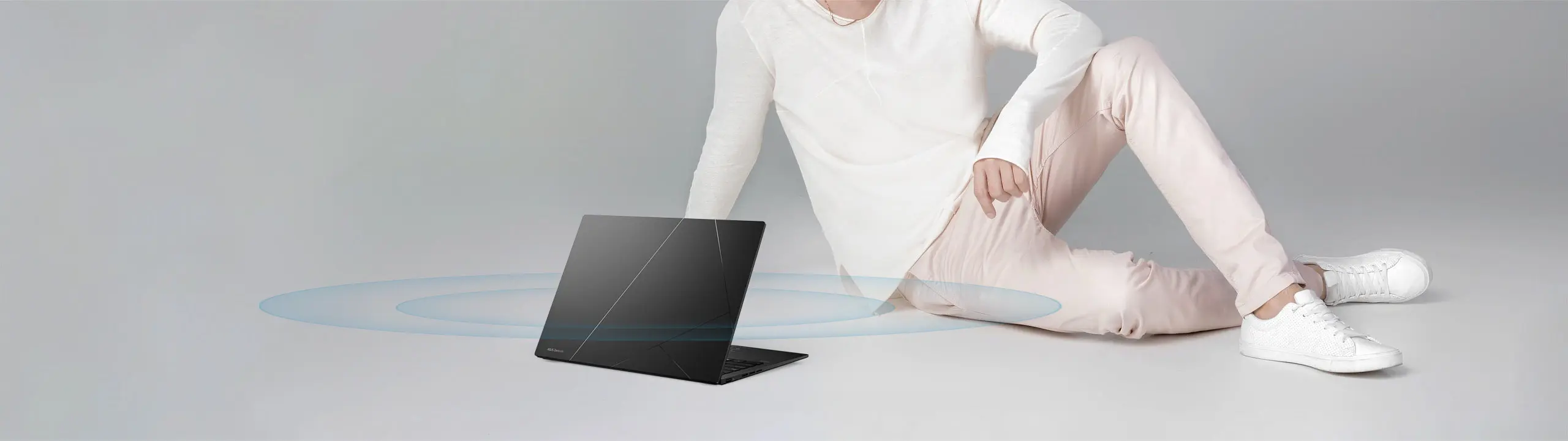 Zenbook 14 OLED laptop is placed on the floor next to a man. The laptop is emmiting sound waves.